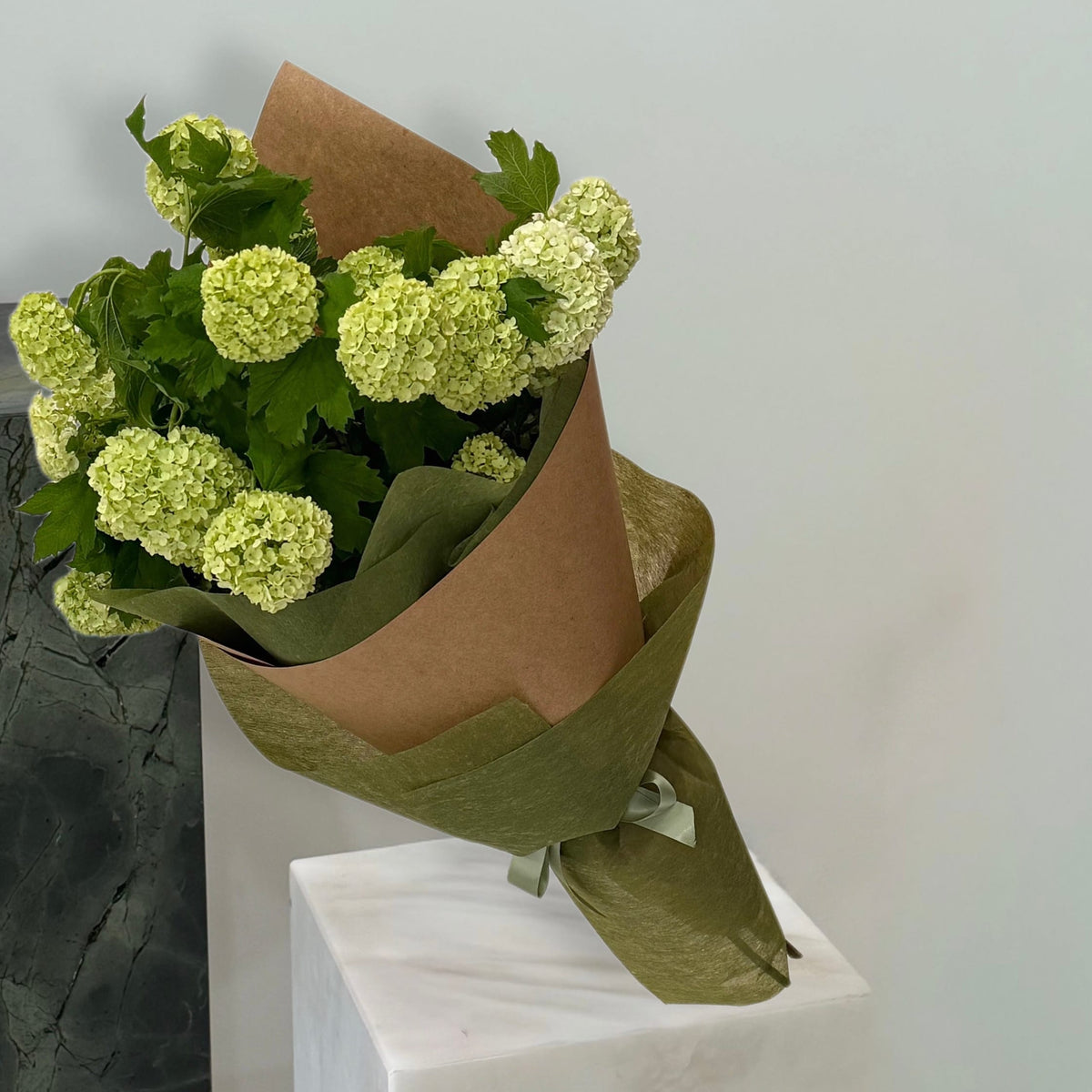 Lime-green snowball bouquet in olive and kraft wrapping with ribbon by Maison Bloomé.