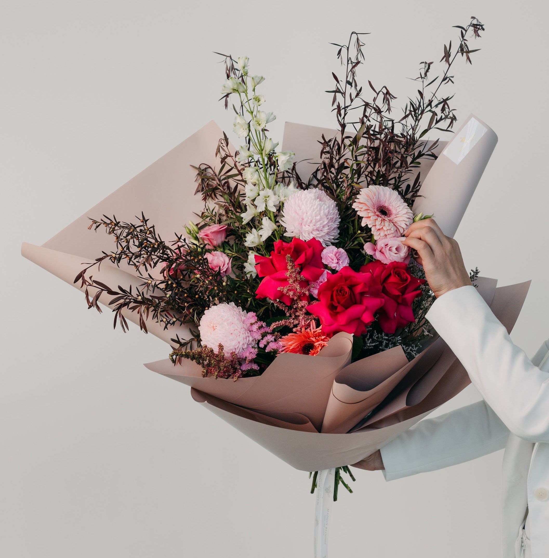 Elegant red and pink flower bouquet wrapped in paper held in hand by Maison Bloomé Adelaide florist
